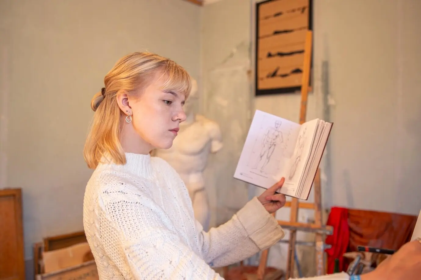 Mujer artista joven y atractiva leyendo un libro de anatomía; concepto de aprendizaje.